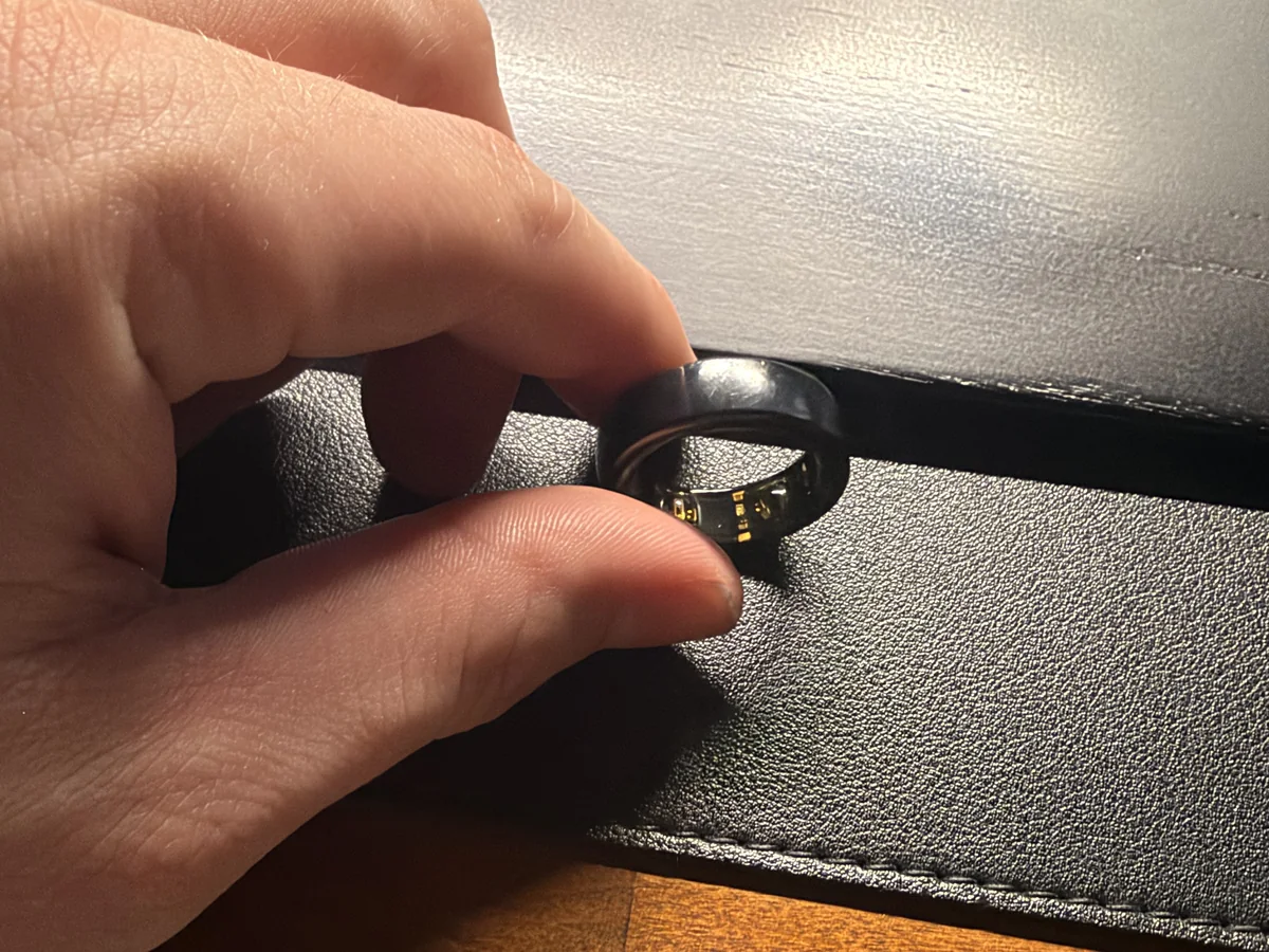 Close-up of our Oura Ring Gen3 held between two fingers, showing scuffs on the black coating and the gold sensor bumps inside